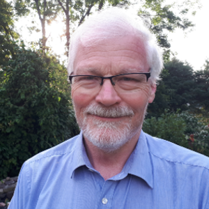 The image shows a man with grey hair wearing glasses and a blue shirt