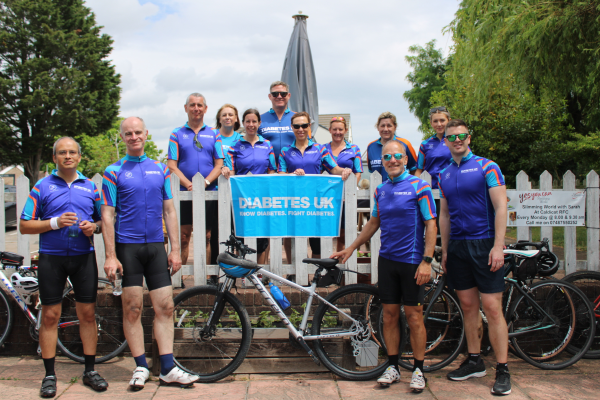 The image shows a group of people wearing Diabetes UK cycling t-shirts holding a Diabetes UK banner.