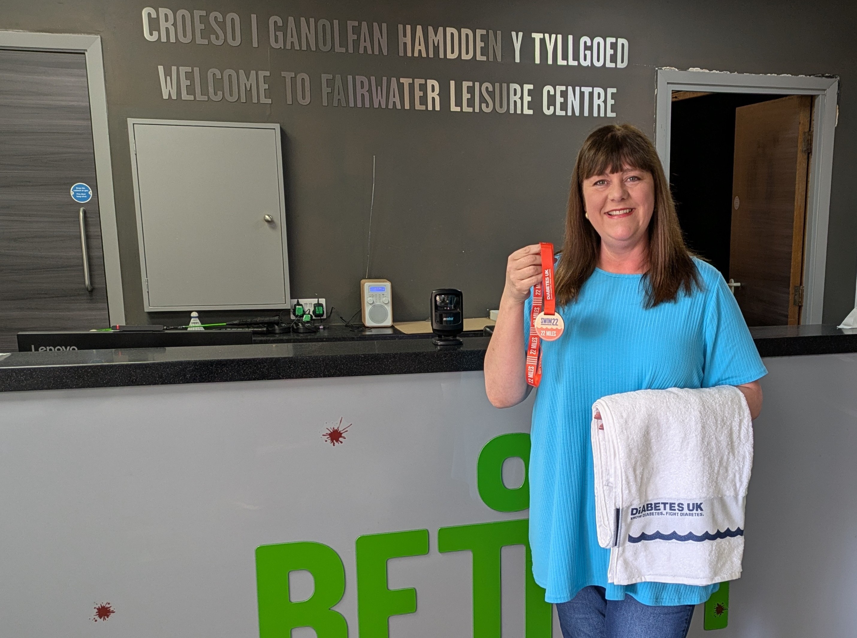 Swim22 participant Julie standing in front of reception desk holding towel and medal