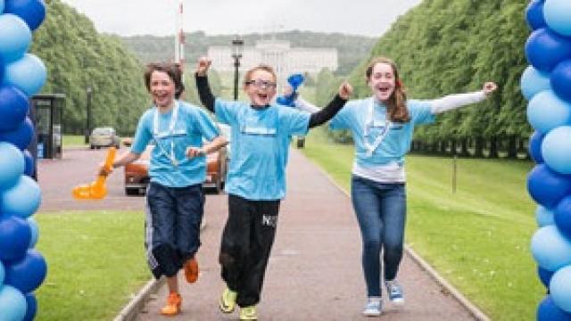 In this image, you can see three women celebrating as they pass through the finish line at one of our fundraising events. They are each wearing pale blue Diabetes UK t-shirts. They are celebrating by holding hands and raising them in the air.