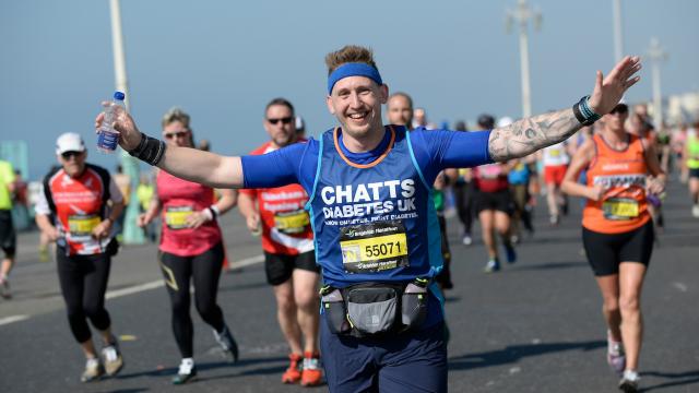 A male runner in a Diabetes UK top smiling as he runs by during a race