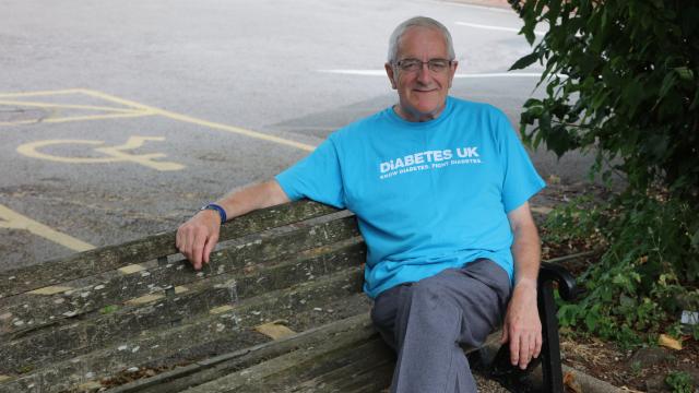 A photo of John sitting on a bench outside, wearing a blue Diabetes UK T shirt