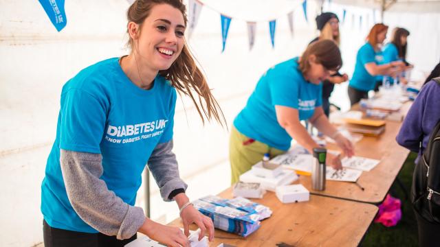 A woman wearing a Diabetes UK t-shirt, standing by a table