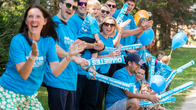 The image shows a group of people in blue t-shirts cheering in the park. 