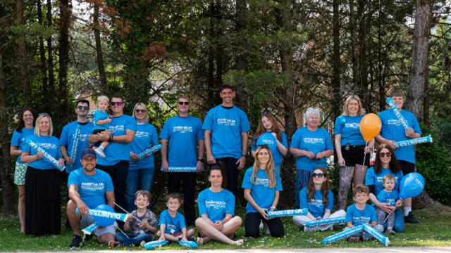 The image shows a group of 21 people wearing blue t-shirts in the park.