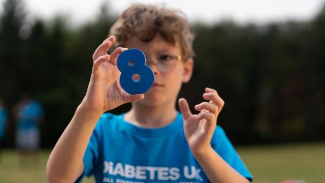 The image shows a young boy wearing a blue Diabetes UK Cymru t-shirt and he is holding a number 8.