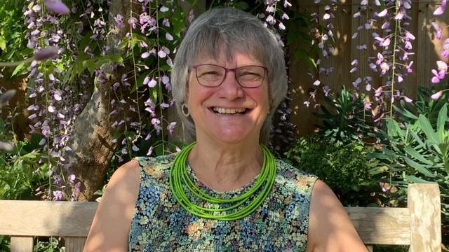 A lady sits on a bench, smiling in the sunshine