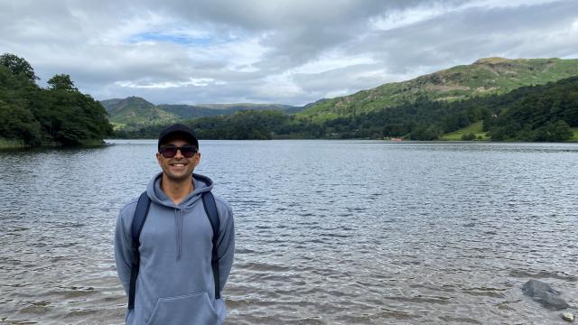 A man stands in front of a lake, smiling at the camera