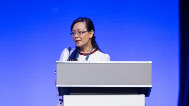 Woman standing at a lectern delivering a lecture.