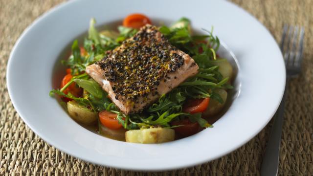 A piece of salmon sits on top of a salad