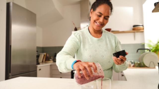 Woman smiling as she pours herself a smoothie