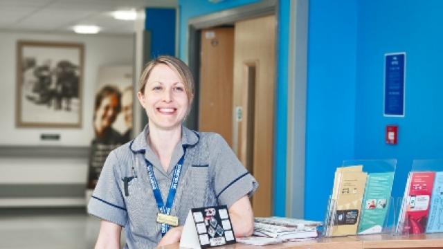 A healthcare professional stands smiling at a reception desk wearing a Diabetes UK lanyard