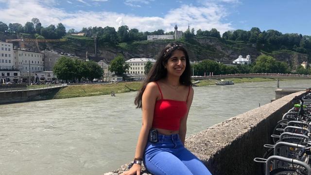 A young woman sits on a wall by a river