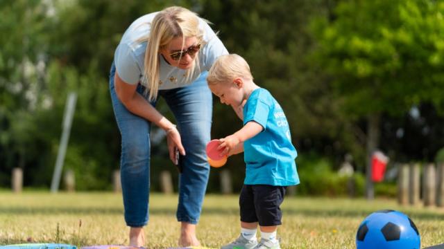 The image shows a lady in the park playing games with a little boy. 