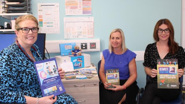 The image shows three ladies in a GP practice. They are each holding a leaflet with information about type 1 diabetes.