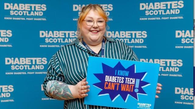 A young woman holds a sign saying 'Diabetes Tech Can't Wait'