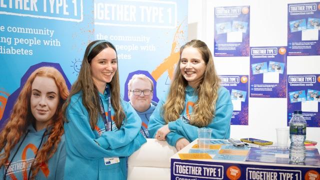 A young leader and Diabetes UK staff member smile at the camera at a Together Type 1 stand