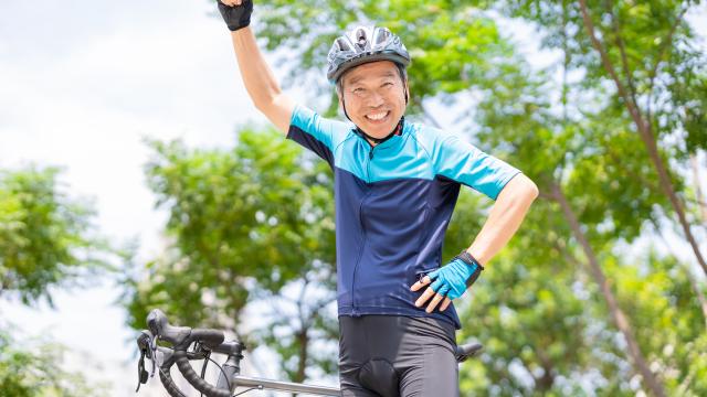 Image of gentleman with arm raised in the air on a bicycle.