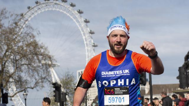 A male runner in front of the London Eyes, with his fist raised in a cheer.