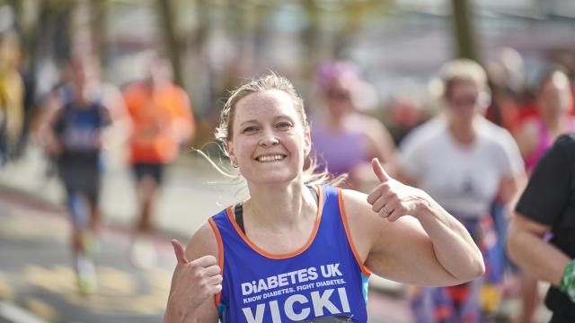 A female runner smiling at the camera with thumbs up.