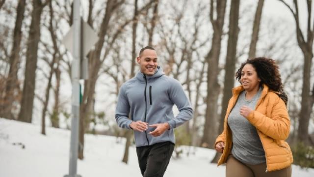 A man and a woman on a jog smiling together through a snowy wooded area