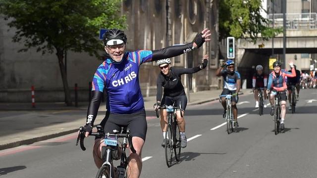 Image of gentleman with arm raised in the air on a bicycle.