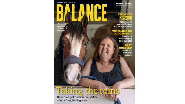 A woman stands next to a brown horse in a stable looking directly into the camera and smiling.