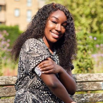 Fatama sitting on a bench smiling and revealing her CGM