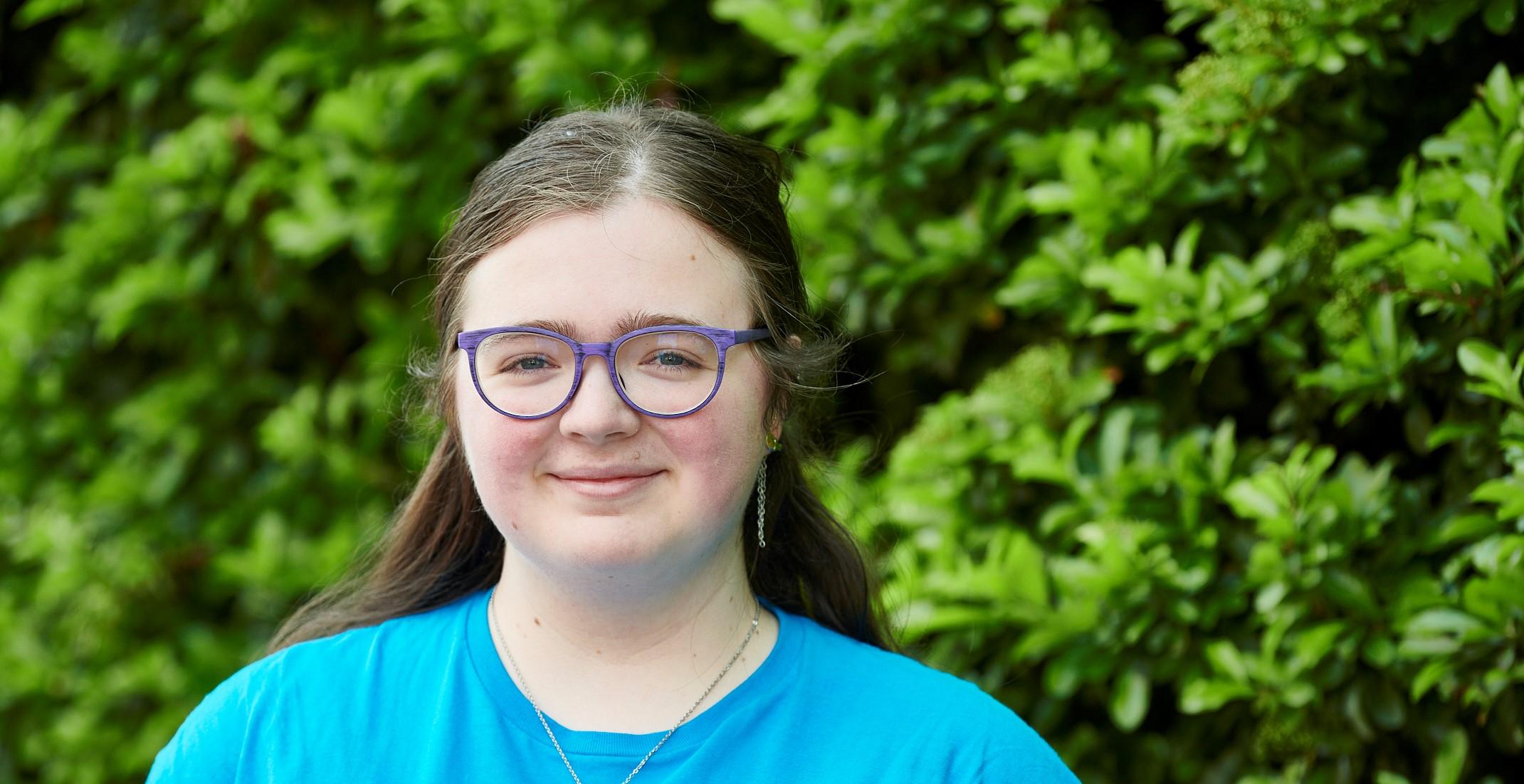 A young woman wearing a blue t-shirt faces the camera