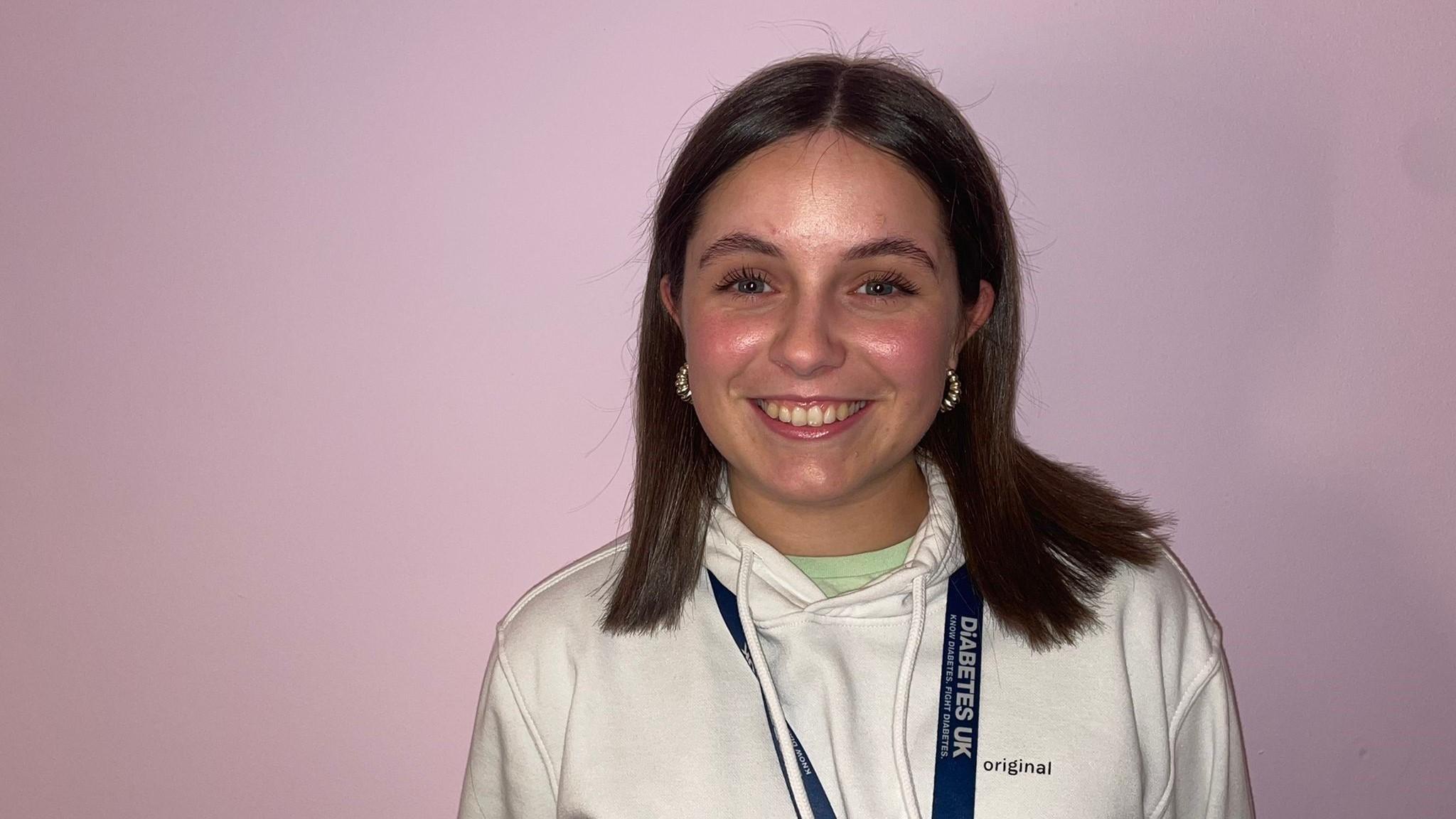 A young woman wearing a white hoody smiles at the camera.