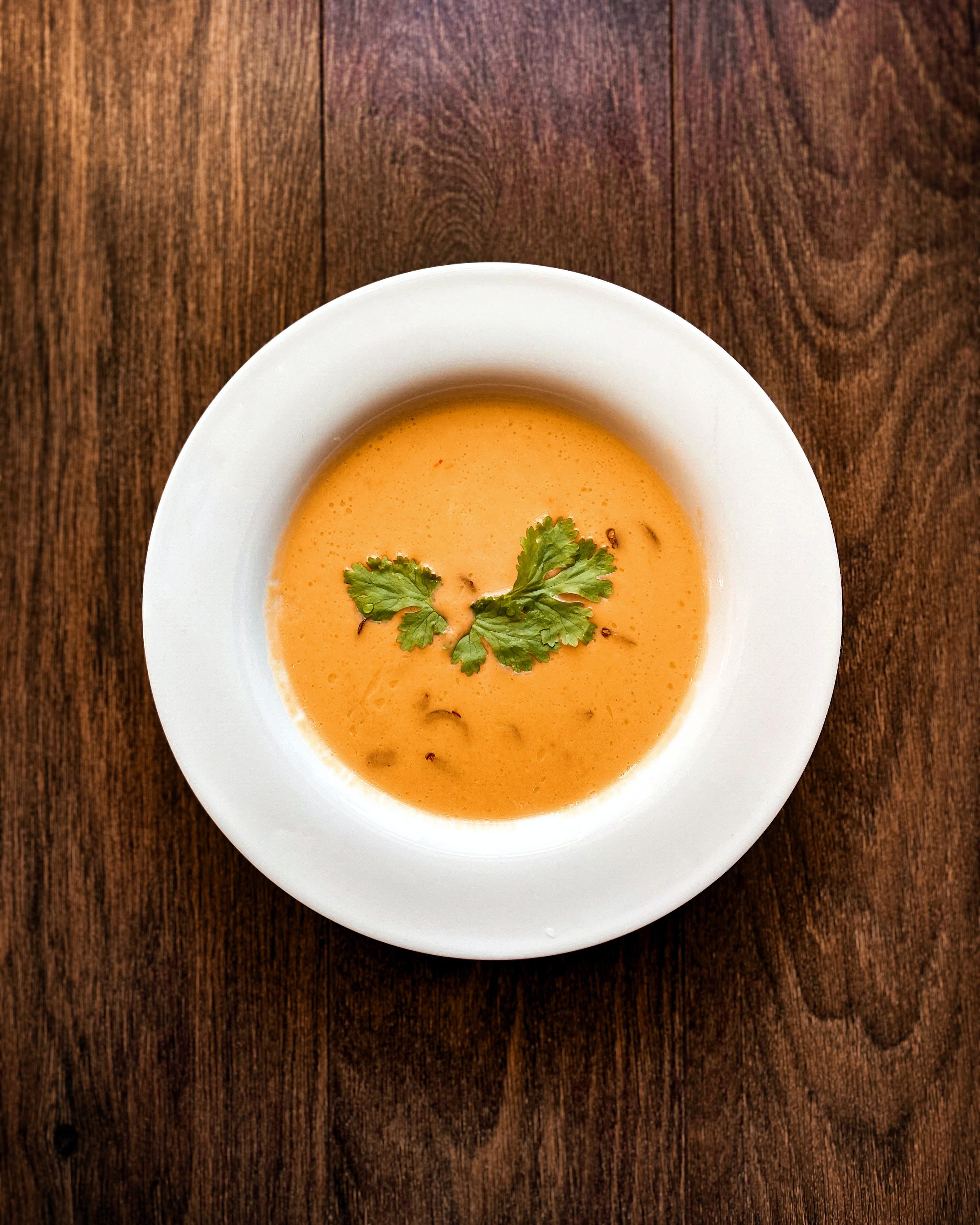 White bowl filled with an orange coloured soup, topped with green herbs.