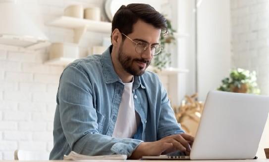 A young man looks at his computer screen sitting at the kitchen counter