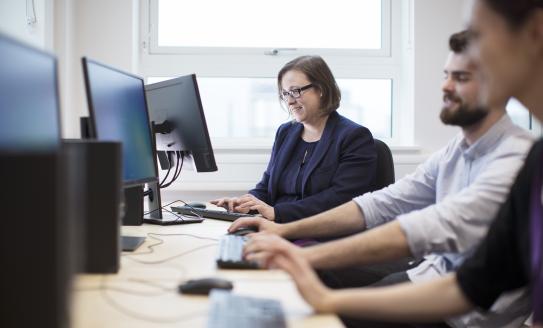 Photo of Professor Claire Meek in black blazer and colleagues working on computer