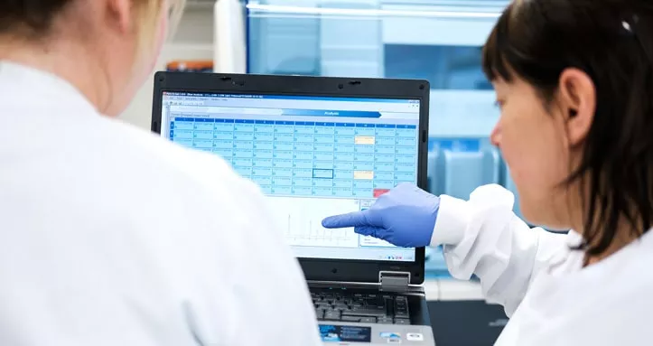 Two scientists in white lab coats with their backs to camera, looking at a computer screen together