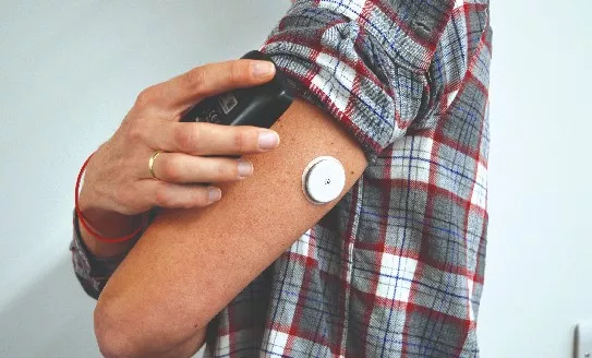 a close up photo of a Flash monitor (A small white circle) on a man's upper arm, which he is scanning with a reader device