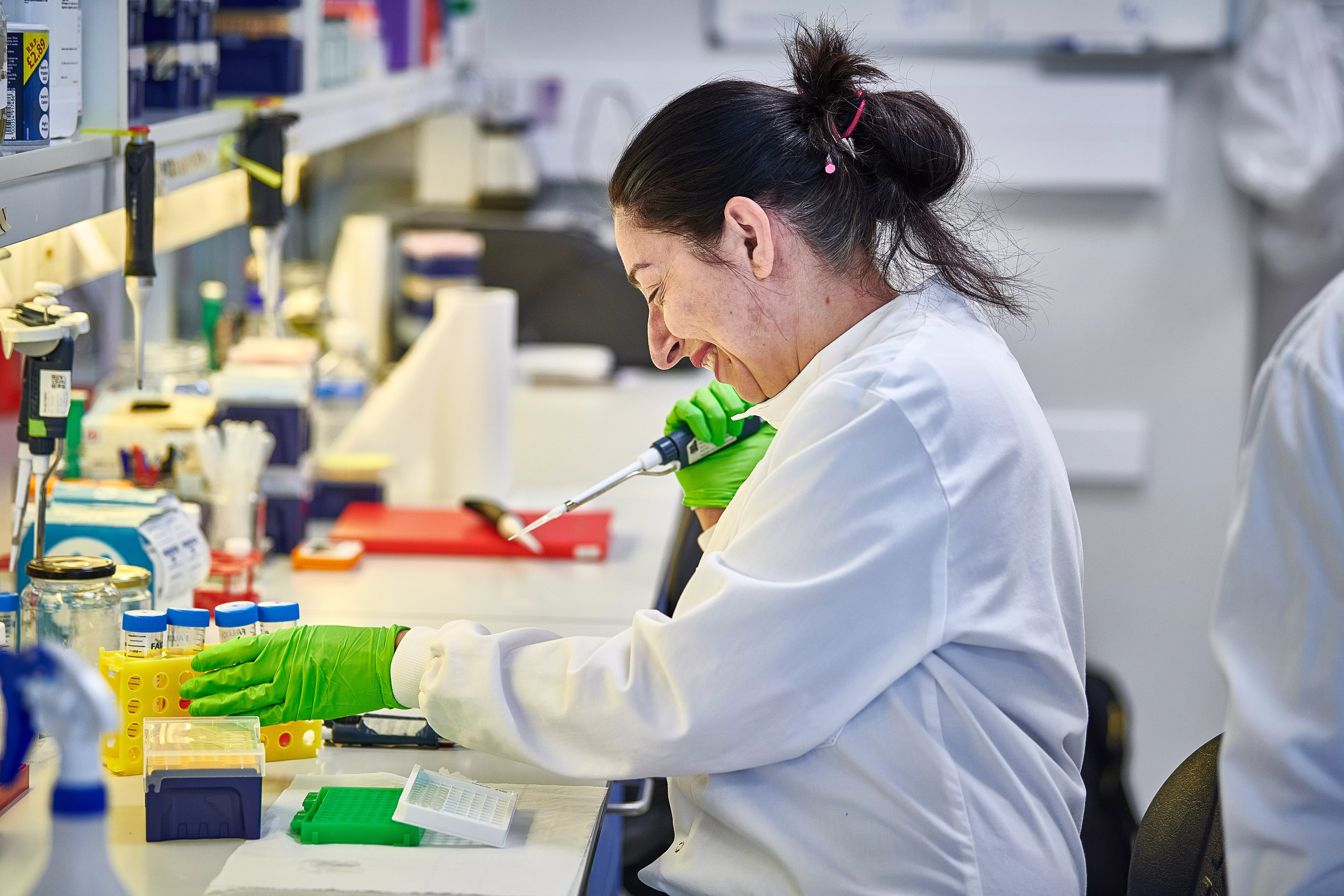 A female scientist wearing a white lab coat and green gloves working in a diabetes lab