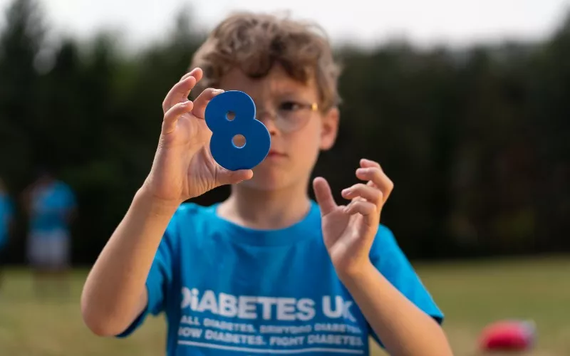 The image shows a young boy in a blue t-shirt holding the number 8.