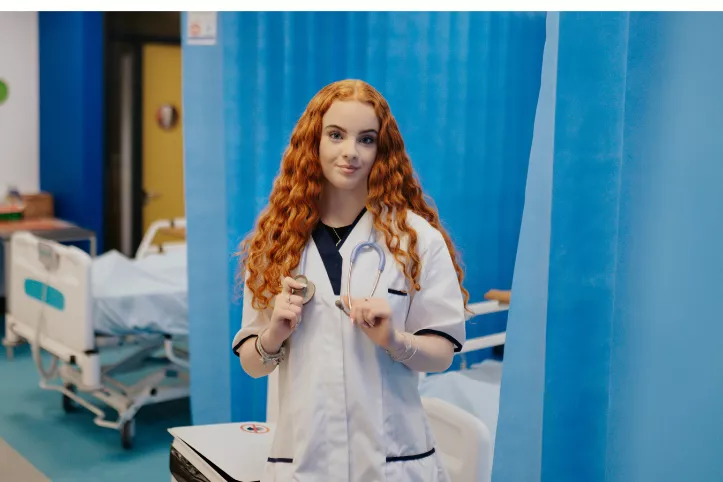 Thalia in a hospital next to a hospital bed in nurse uniform