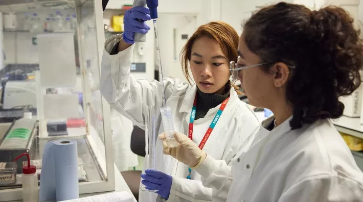 Two researchers in lab coats testing a liquid in a test tube.