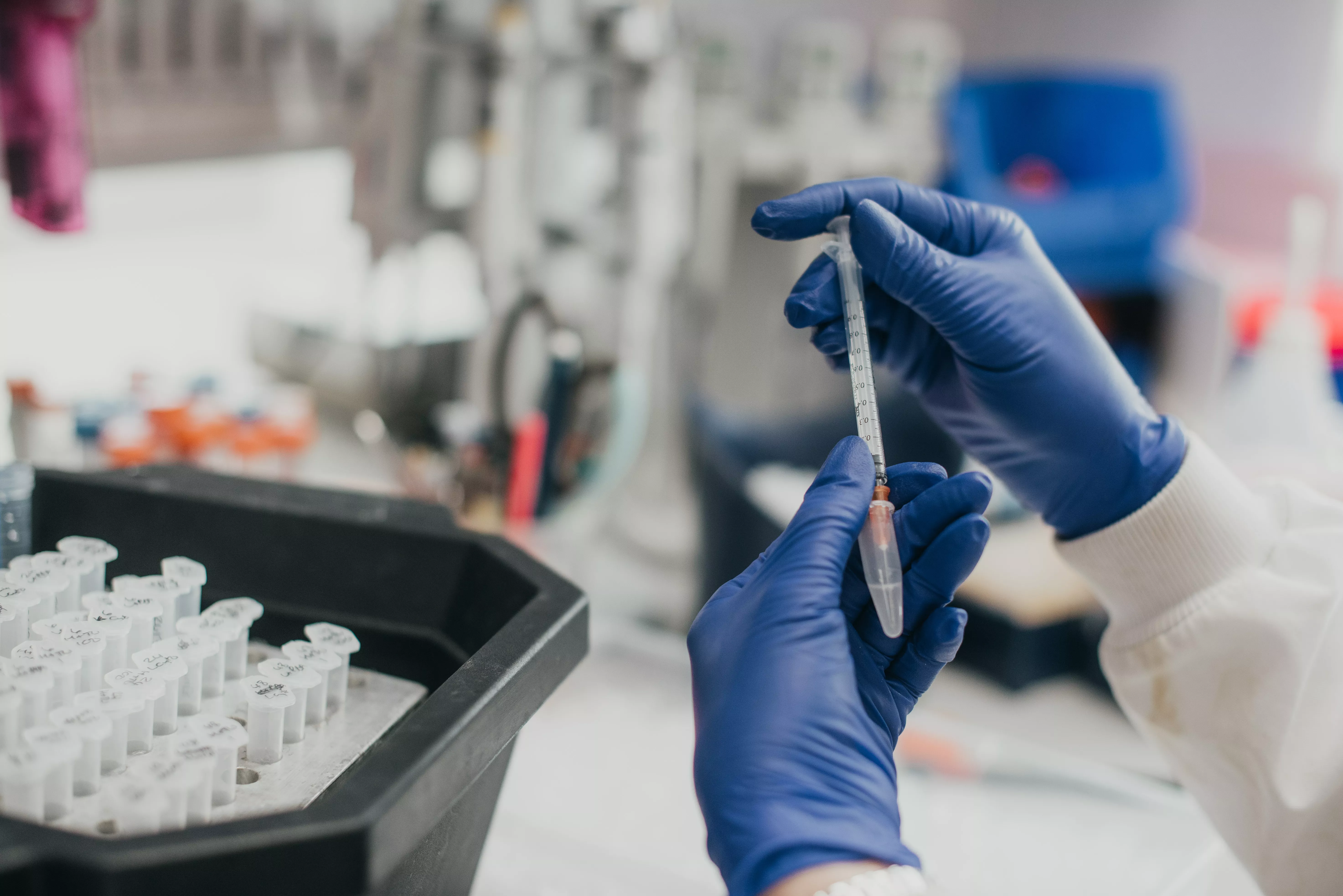 Photo of hands in blue gloves holding a syringe and eppendorf tube