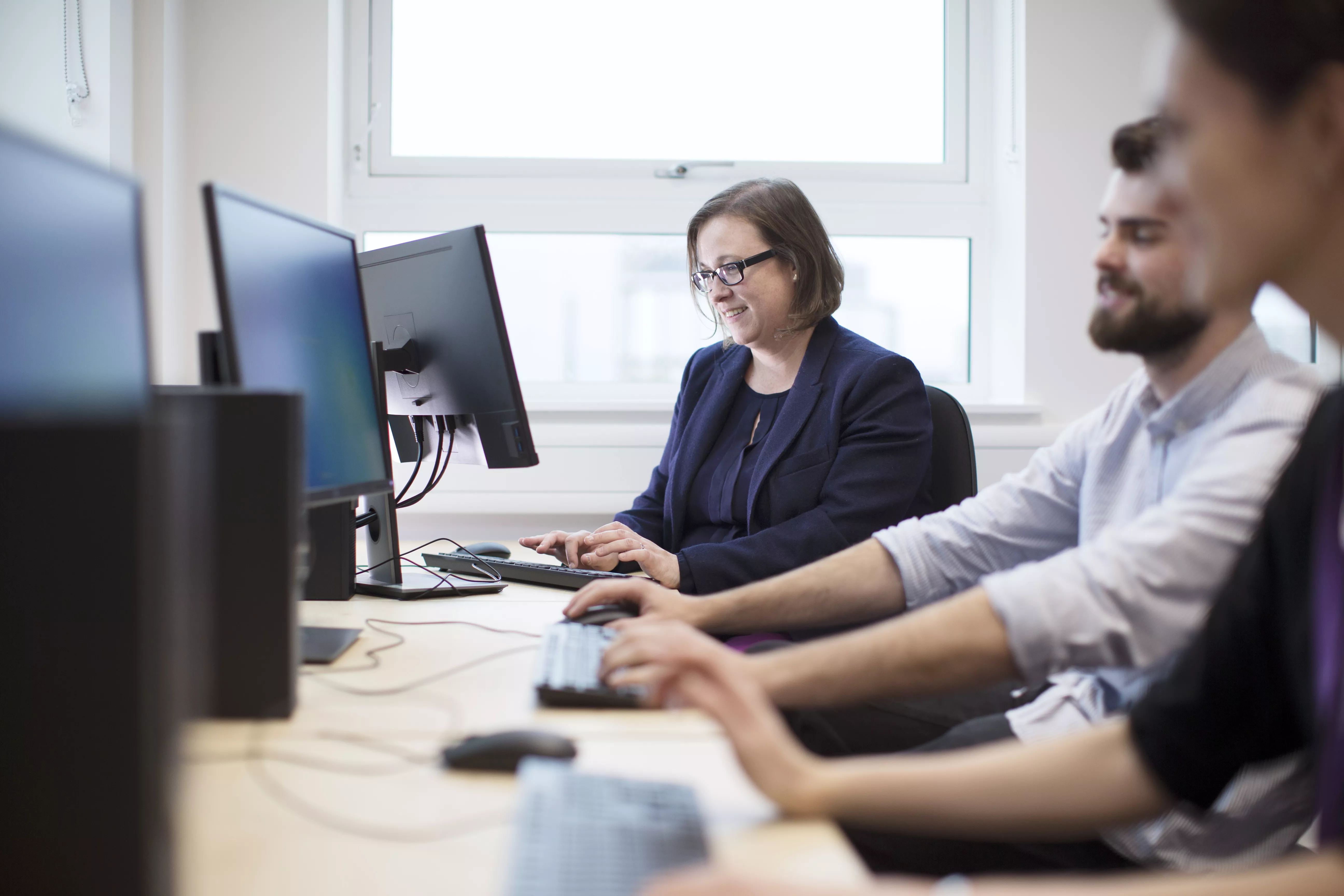 Photo of Professor Claire Meek in black blazer and colleagues working on computer