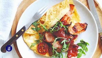 A sausage bacon omelette next to some salad on a plate