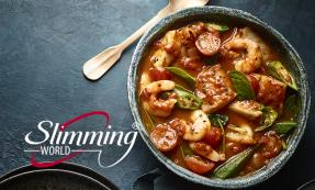 Reddish seafood curry with green chillies and spinach in a stone bowl on slate