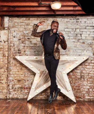 Young black man wearing sparkly suit and singing into a microphone in a jump 