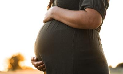 A heavily pregnant woman in a green dress holding her bump against a sunset background