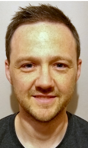 A headshot of Paul Niven, a Caucasian man with dark hair, wearing a navy blue top, smiling to camera