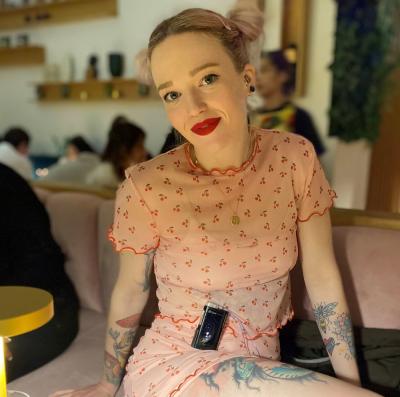 A photo of Laura, wearing a pink dress and red lipstick, facing the camera with her insulin pump visible