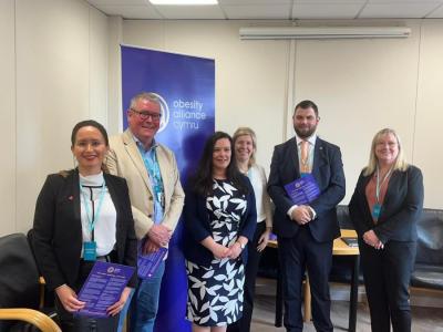 The image shows a group of six people smiling for a photo in the Senedd