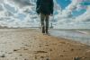 Man seen from the back is walking along a sandy beach. The sky is blue.